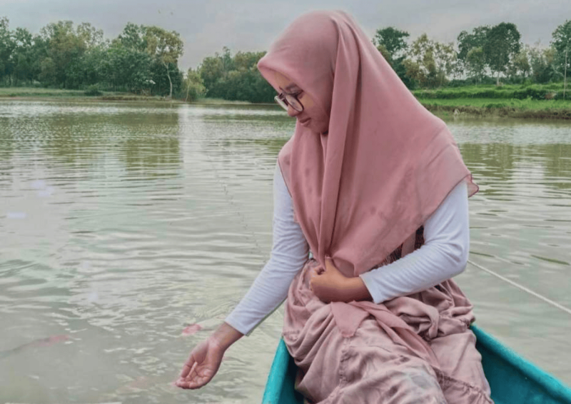 Seorang pegunjung sedang bermanja ria dengan ikan koi di Wisata Ikan Koi Lebeng Timur (Foto: Ist)